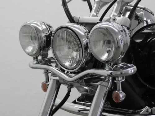 Drei verchromte Scheinwerfer an einem Motorrad mit einem stabilen Halter und Kabelverbindungen.